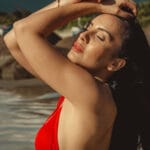 Woman in a red bikini posing for a photo with her hands on her face.