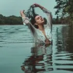 Woman in a white shirt posing for a creative portrait in the water with wet hair.