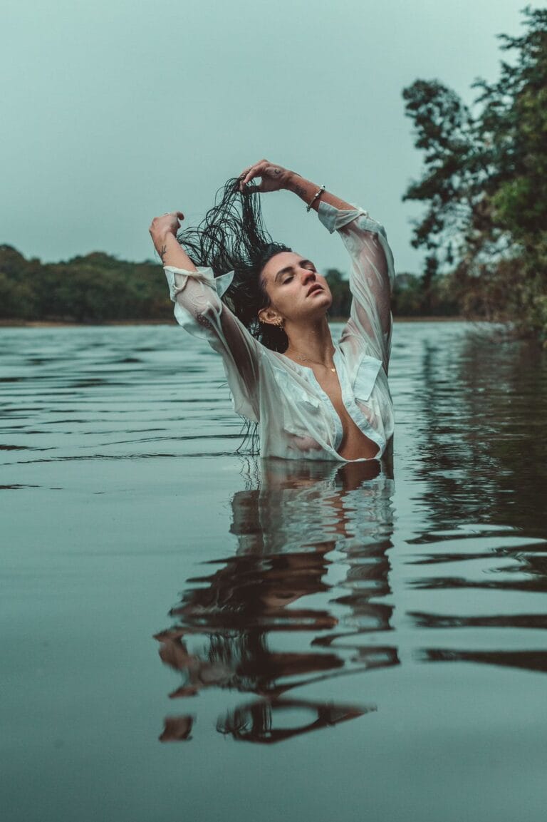 Woman in a white shirt posing for a creative portrait in the water with wet hair.