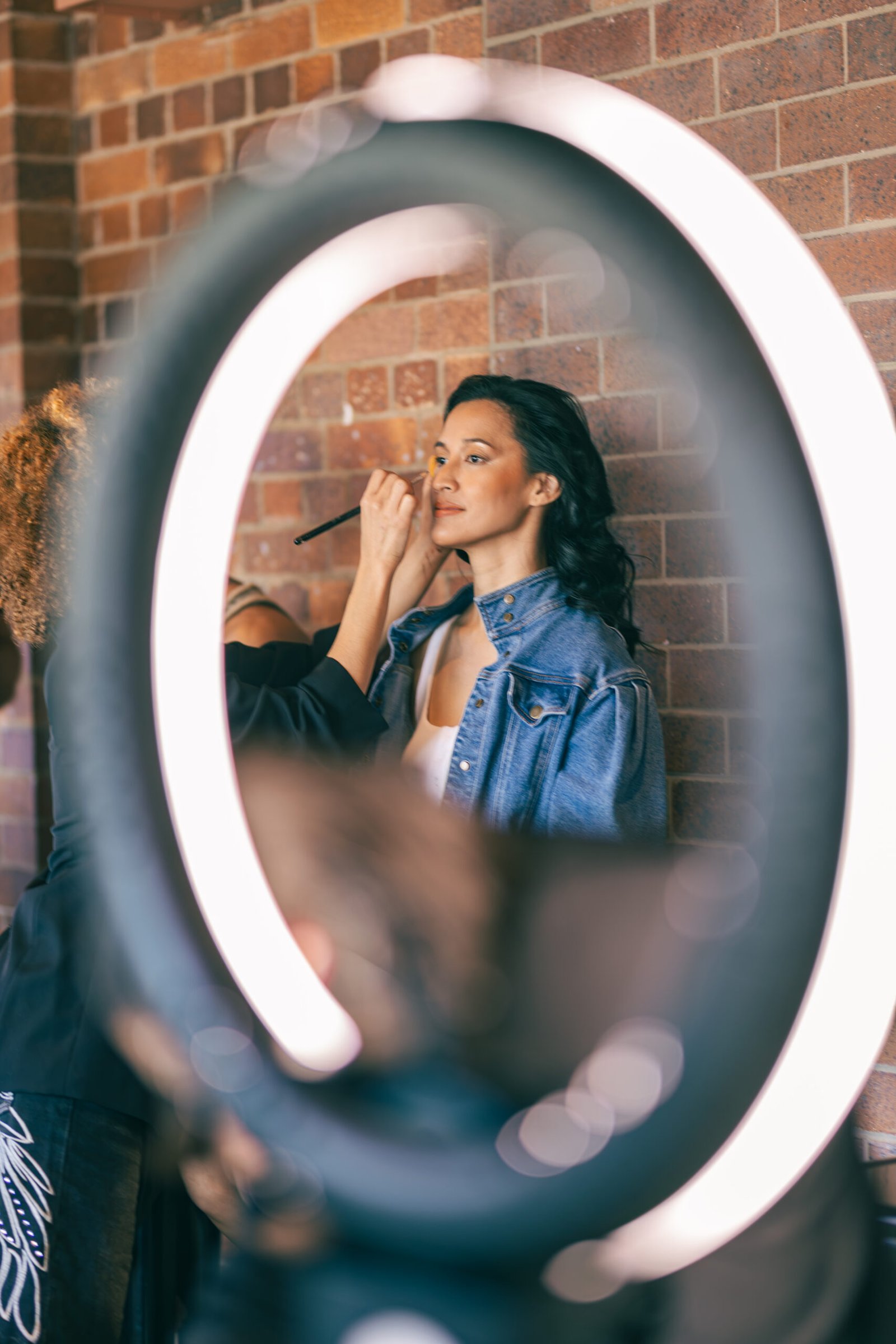 Makeup artist working under a ring light before the runway